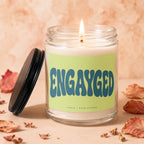 Glass jar candle with lit wick and "ENGAYGED" text on label.
