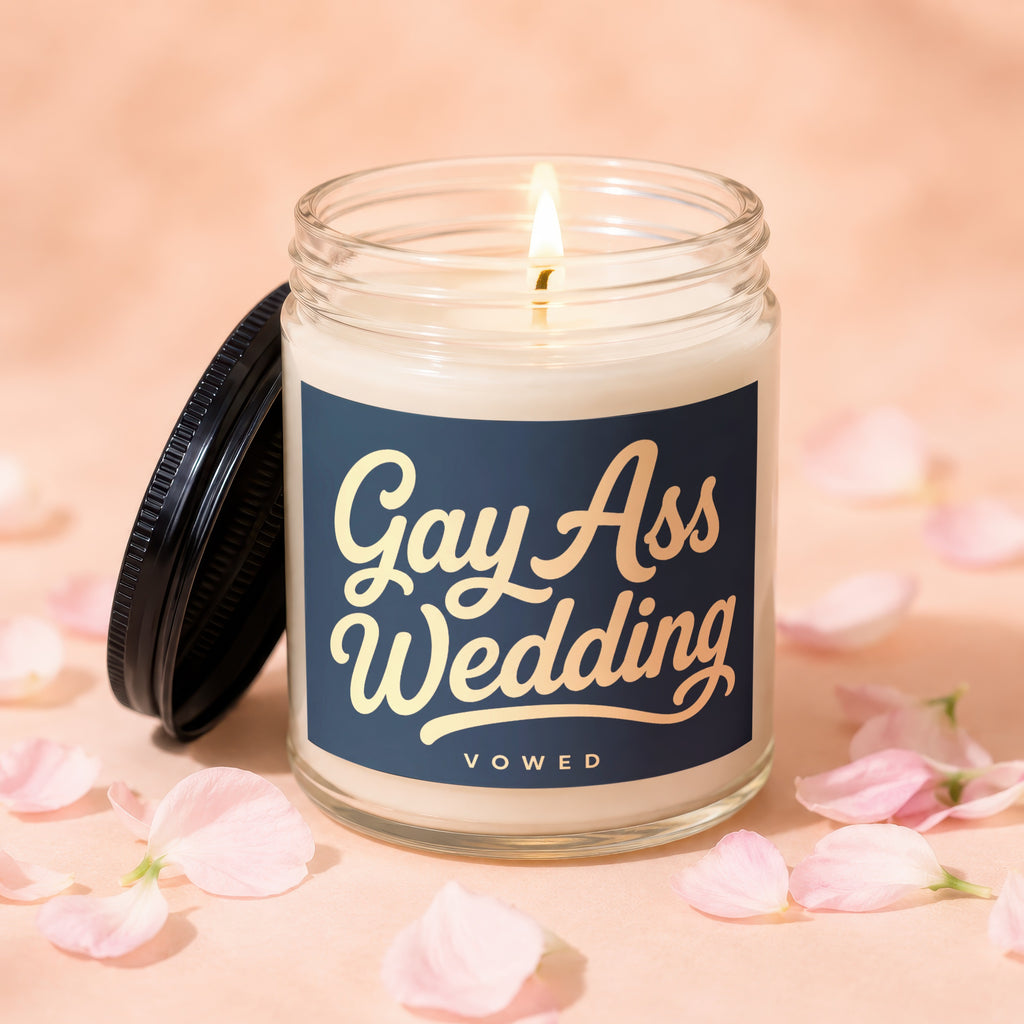 Candle with "Gay Ass Wedding" text, lit flame, black lid, and scattered petals.