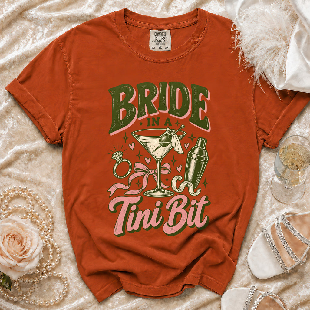 Orange t-shirt with "Bride In A Tini Bit" text, cocktail, and ring graphics.