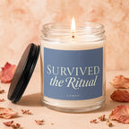 Candle with blue label reading "SURVIVED the Ritual" and "VOWED", with lit wick.