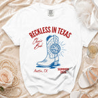 White t-shirt with "Reckless in Texas" graphic, cowboy boot, disco ball, Austin TX, Summer 2026.