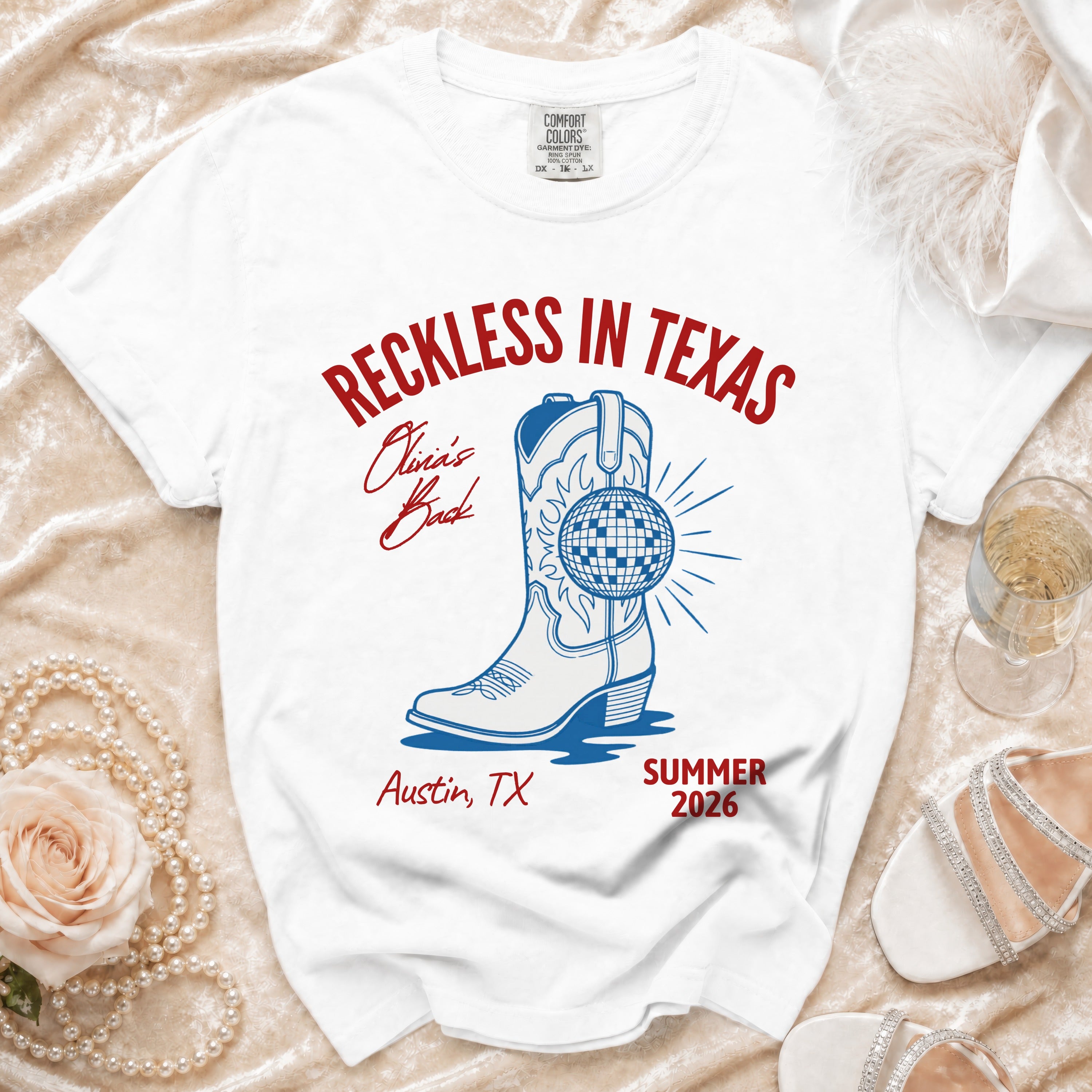 White t-shirt with "Reckless in Texas" graphic, cowboy boot, disco ball, Austin TX, Summer 2026.