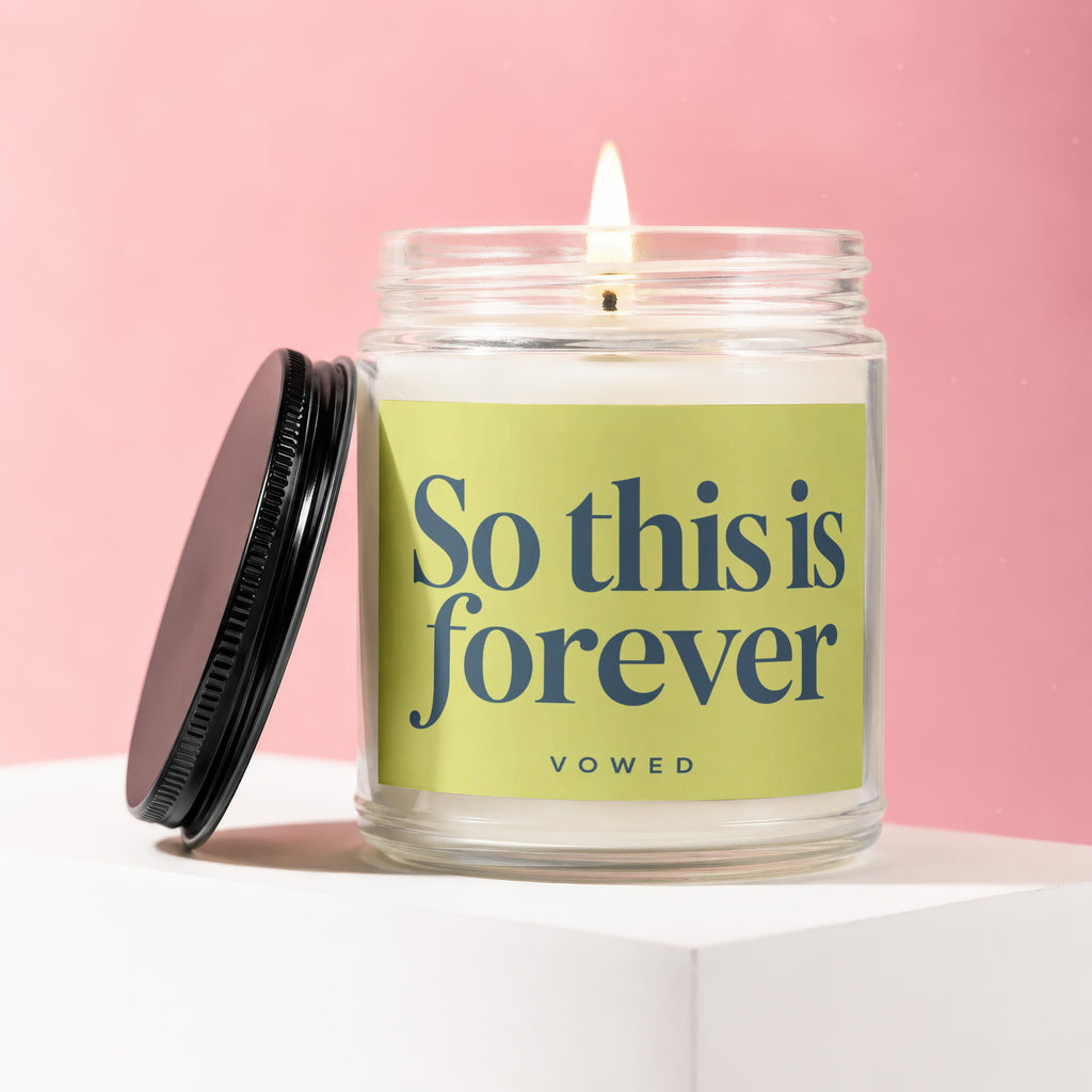 Candle labelled "So this is forever" from Vowed, with lid removed, on a white surface.