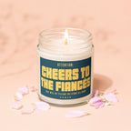 Candle with gold text: "Attention: Cheers to the Fiances", pink petals scattered.