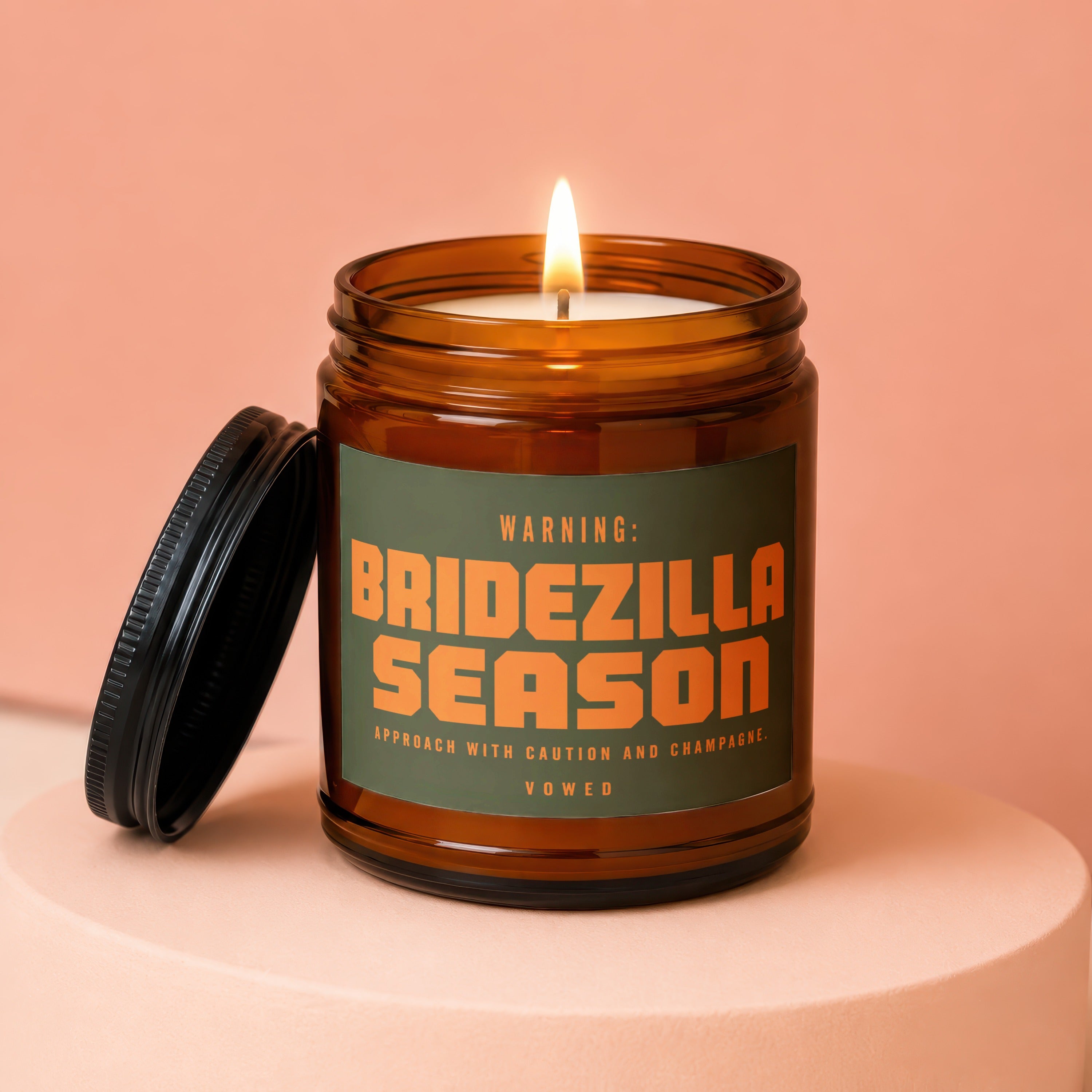 Amber jar candle with lit wick and lid off, labeled "BRIDEZILLA SEASON"
