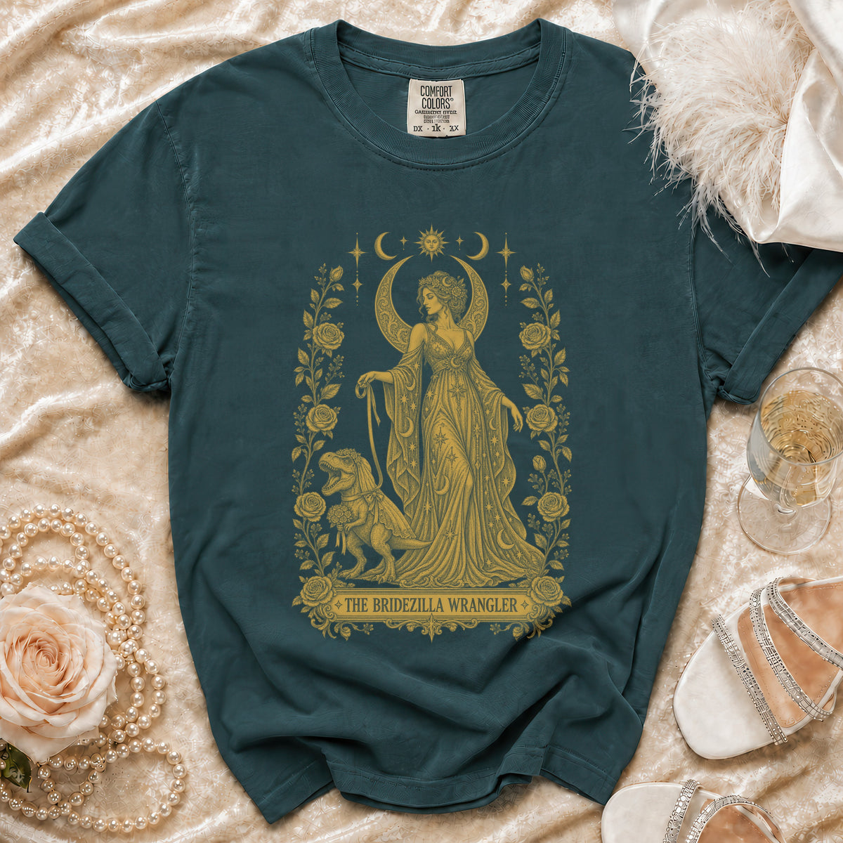 Dark green t-shirt with gold graphic of woman and dinosaur, reading "The Bridezilla Wrangler".