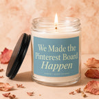 Glass candle with lit wick, blue label reading "We Made the Pinterest Board Happen".