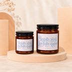 Two amber glass candles with black lids, labeled "Legally wed, joyfully queer"