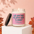 Glass jar candle with pink label reading "will you hold my dress while I pee?"