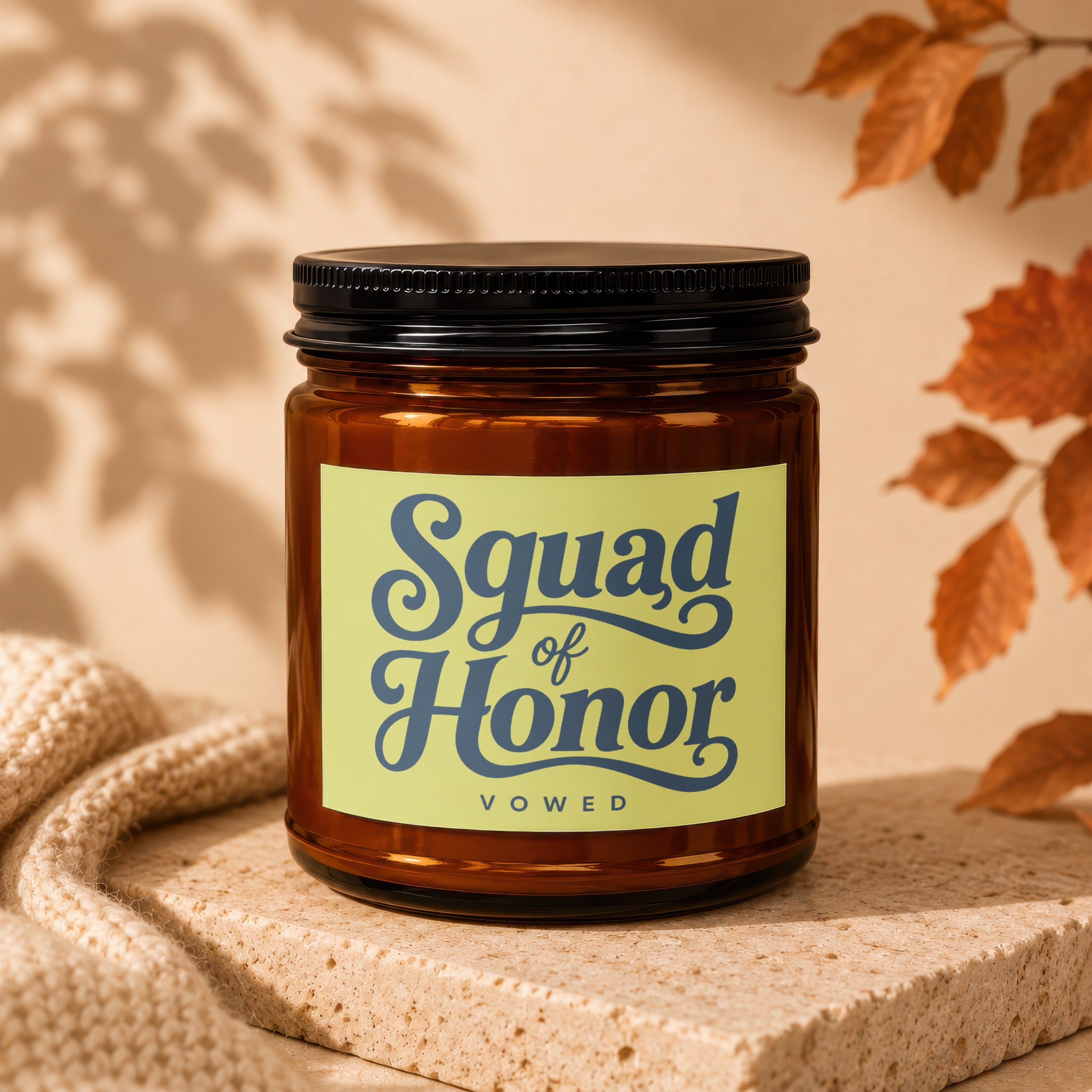 Amber candle with "Squad of Honor VOWED" label on a textured block with autumn leaves.