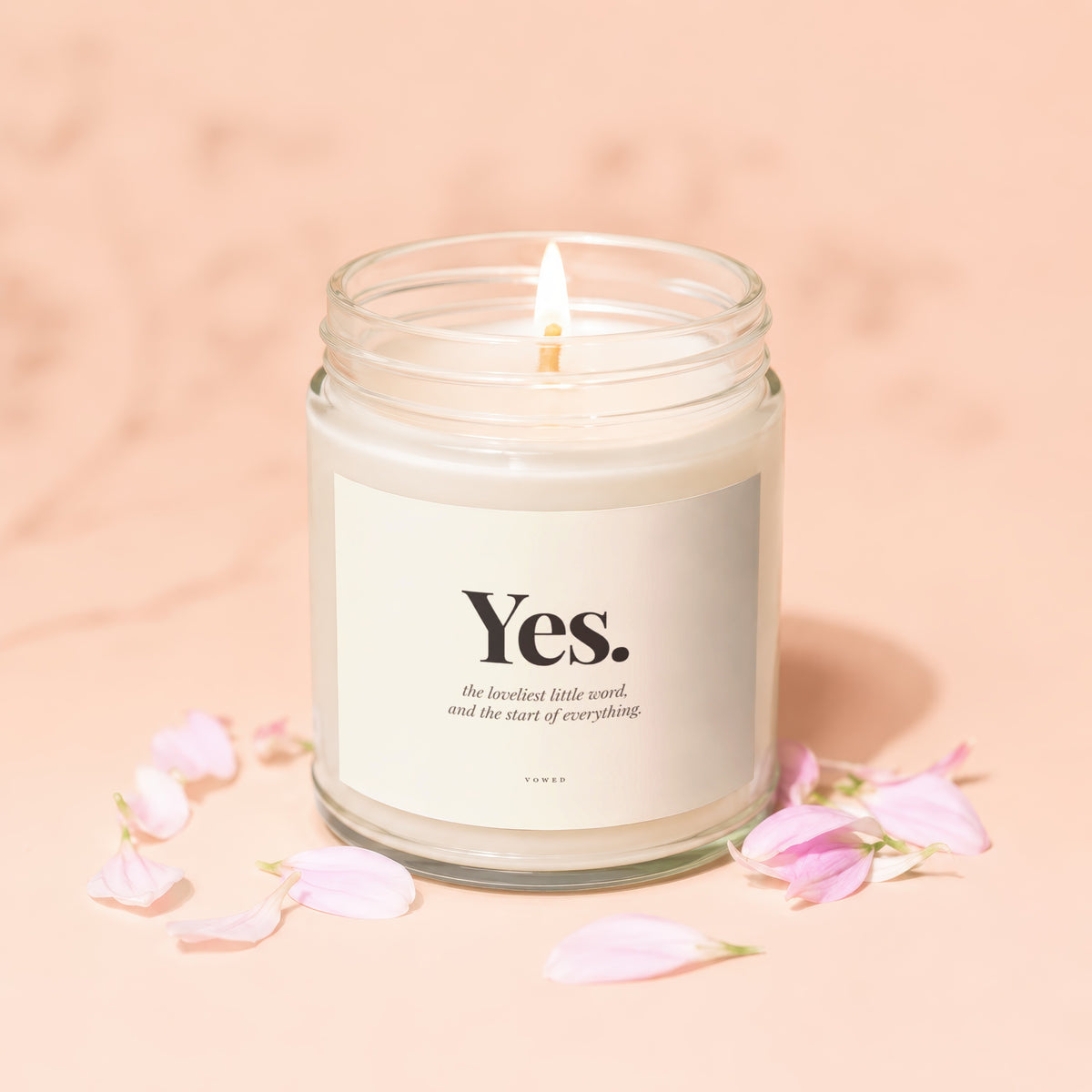 Lit candle with "Yes." and quote on label, surrounded by pink flower petals.