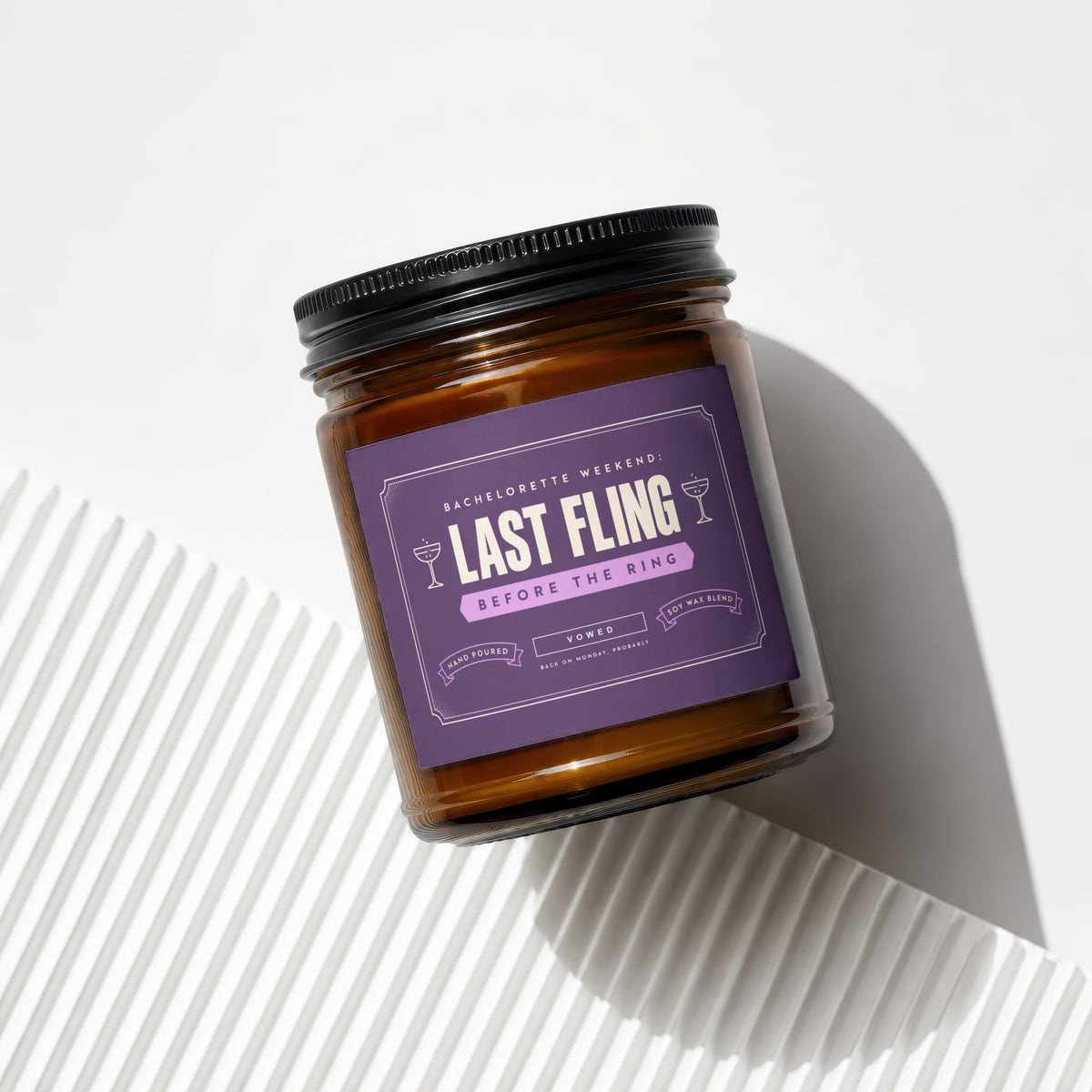 Amber glass candle with purple label reading "Last Fling Before the Ring".