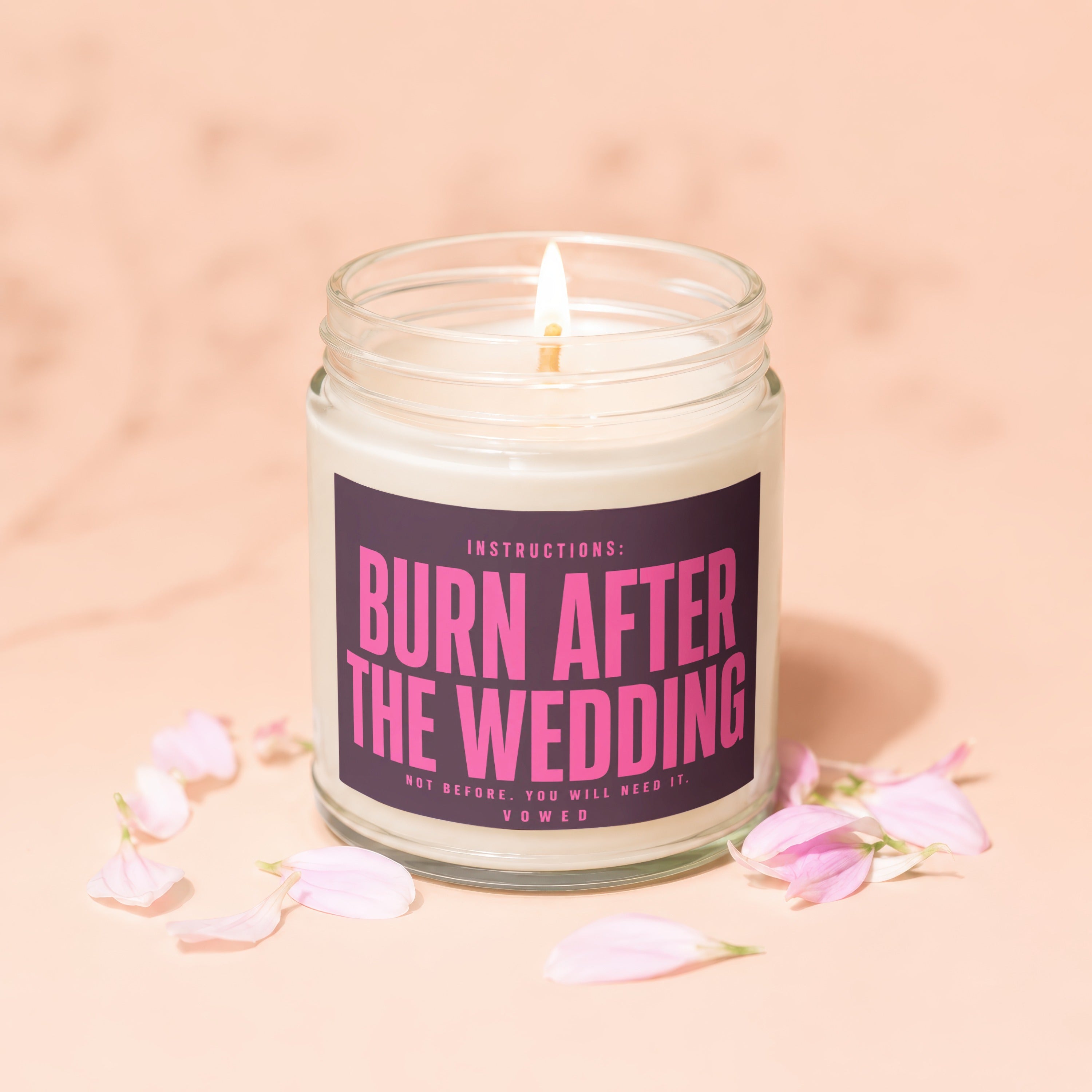 Candle with "Burn After The Wedding" text and scattered pink flower petals.