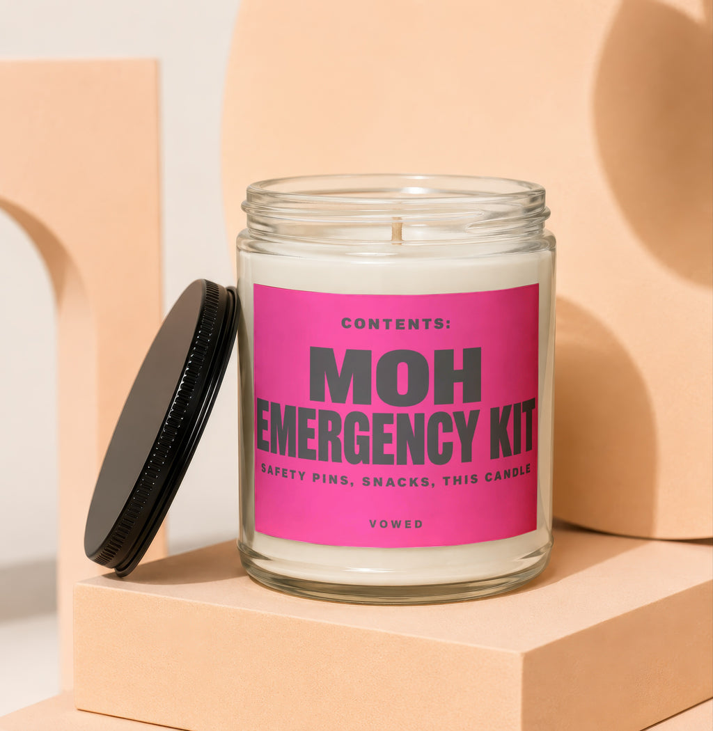 Glass jar candle with pink label: MOH Emergency Kit, Safety Pins, Snacks, This Candle, Vowed.