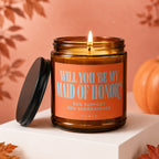 Amber candle with lit wick and lid nearby, reading "Will You Be My Maid of Honor?".