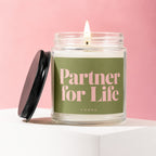Glass candle with lit wick and lid off, reading "Partner for Life."