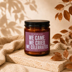 Candle with text "We Came. We Cried. We Celebrated." on a textured surface.