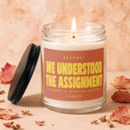Lit candle with "We Understood the Assignment" text on a brown label.