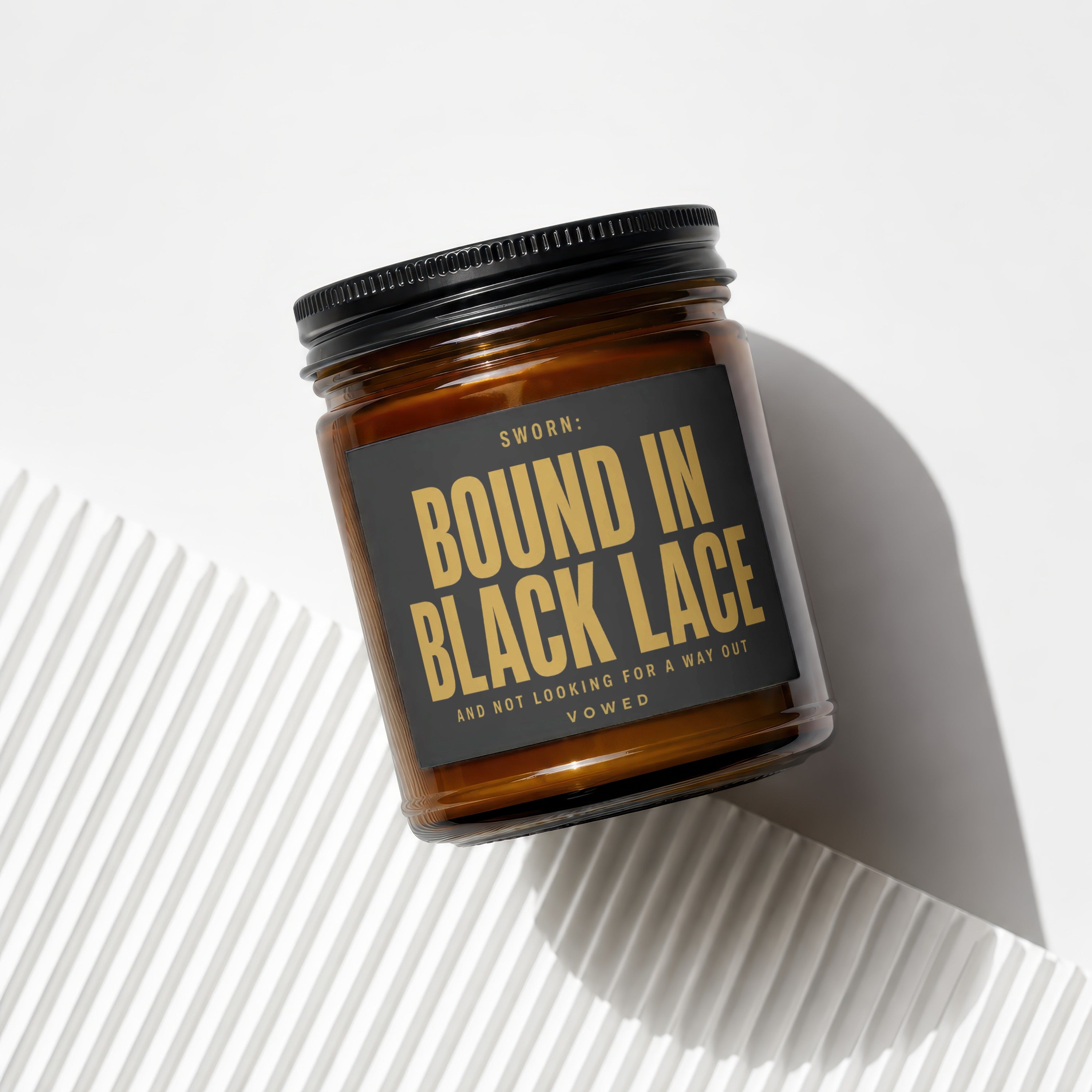 Amber jar candle with black lid, label reads "SWORN: BOUND IN BLACK LACE AND NOT LOOKING FOR A WAY OUT VOWED".