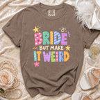 Brown t-shirt with colorful "BRIDE BUT MAKE IT WEIRD" text and bridal accessories.