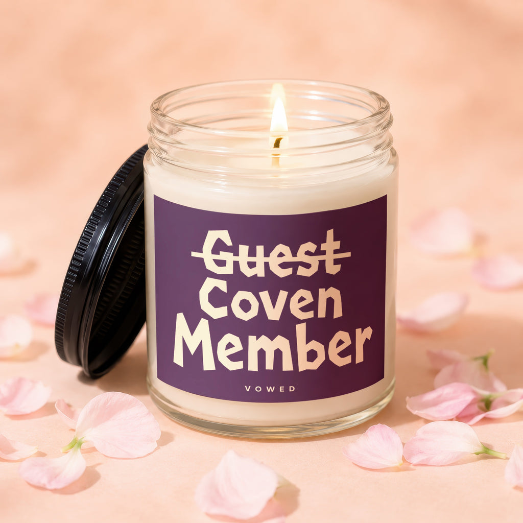 Candle with "Guest Coven Member" text on a dark purple label, lit flame.
