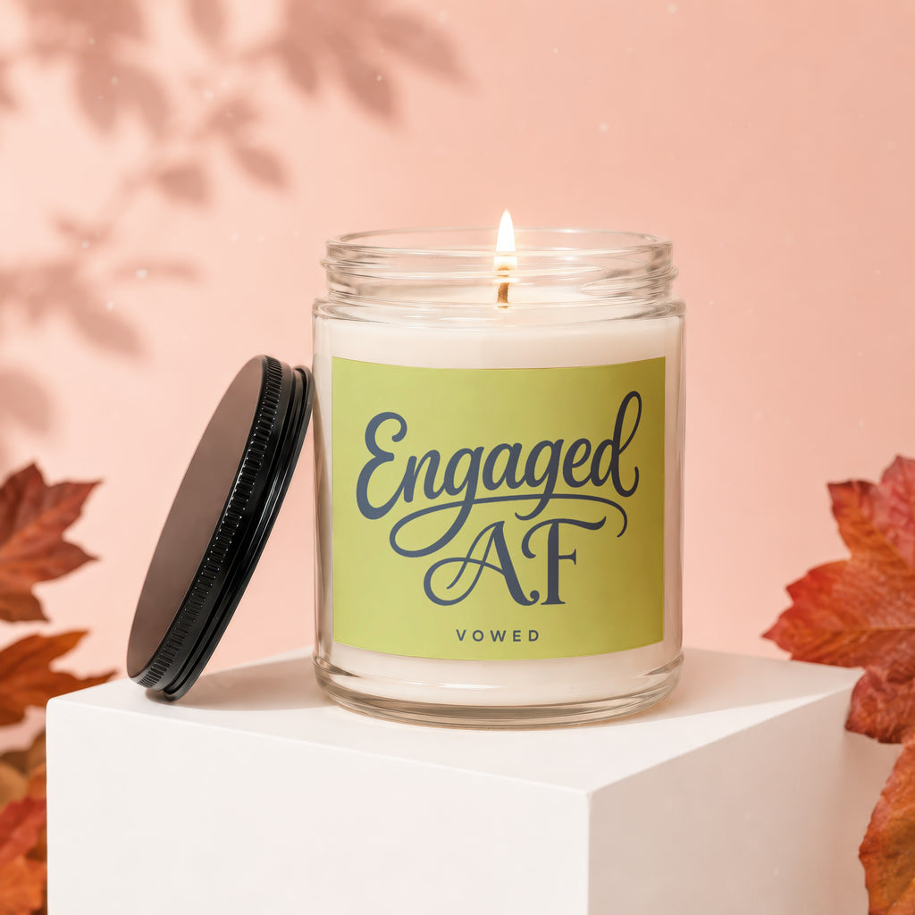 Candle with "Engaged AF VOWED" text on a soft pink backdrop, beside fall leaves.