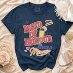 Navy t-shirt with text "Maid of Honour Needs A Mimosa" and a champagne glass graphic.