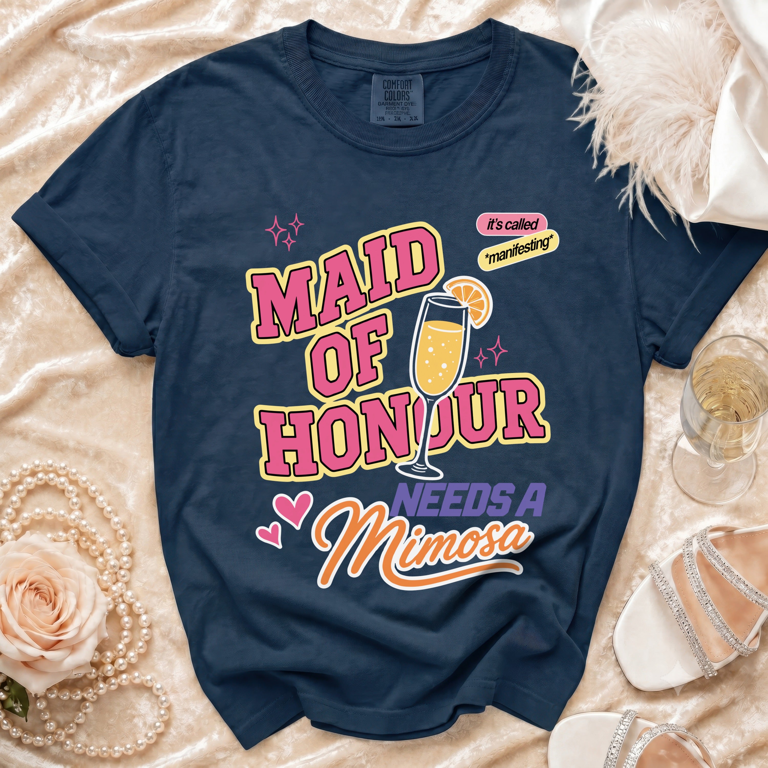 Navy t-shirt with text "Maid of Honour Needs A Mimosa" and a champagne glass graphic.