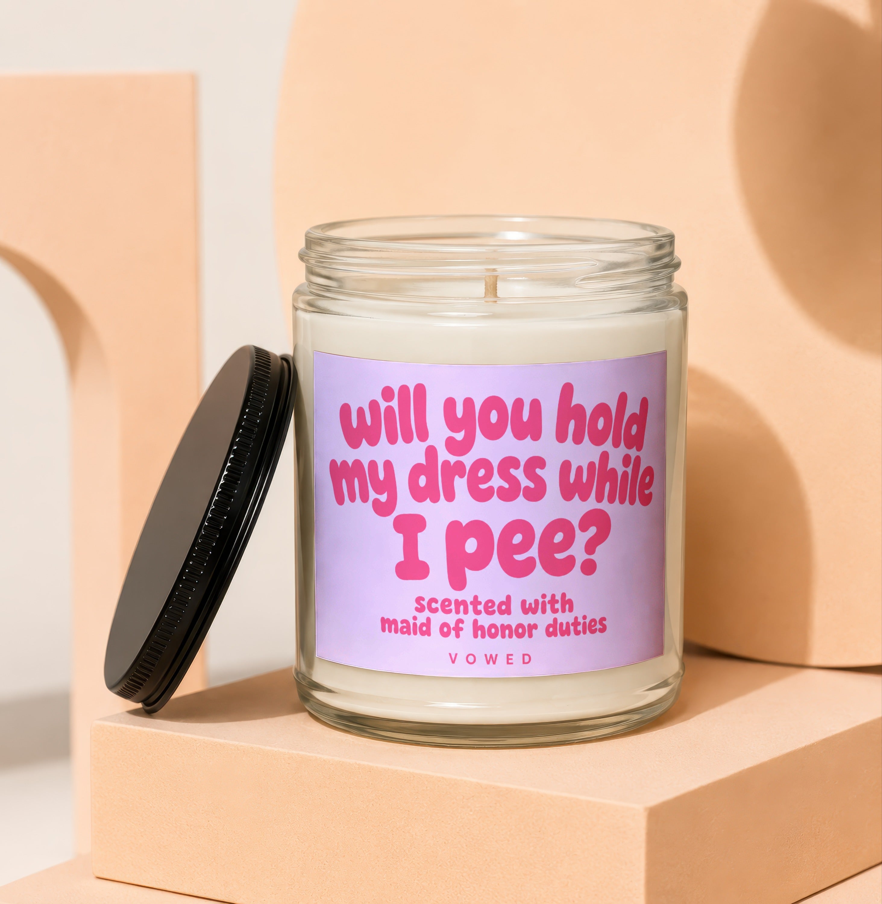 Glass jar candle with pink text asking "will you hold my dress while I pee?".