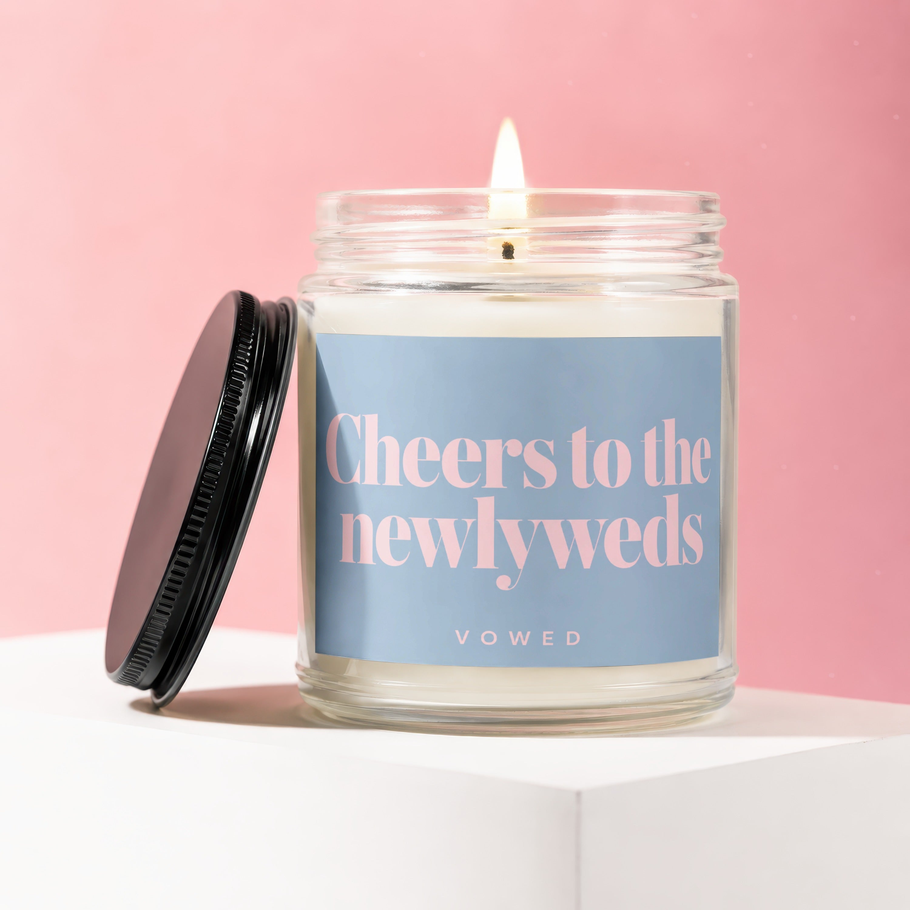 Lit candle in glass jar with "Cheers to the newlyweds" on label.