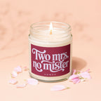 Jar candle with a lit wick and a label reading "Two Mrs, no mister"
