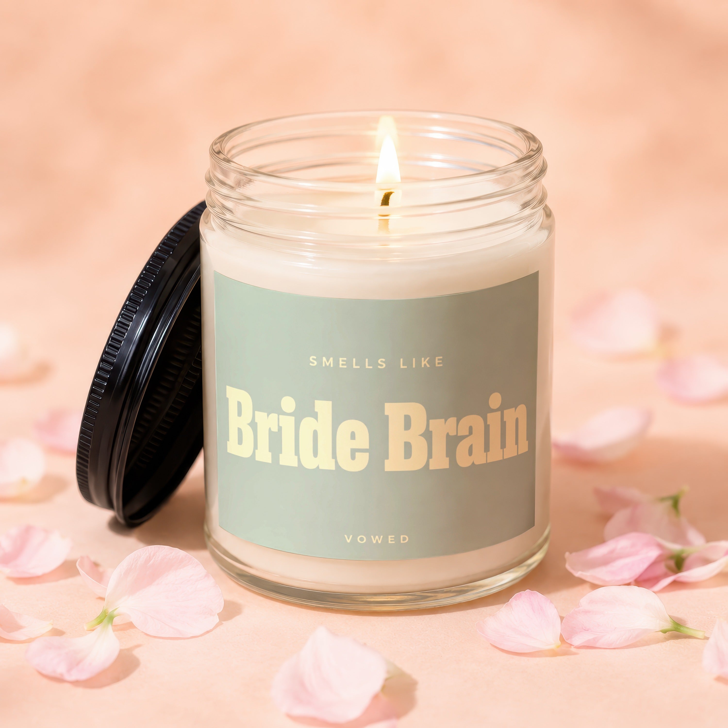 Lit glass candle with a label reading "Smells Like Bride Brain Vowed" on pink background.