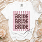 White t-shirt with "Bride to be Bride" text on a pink stripe background.
