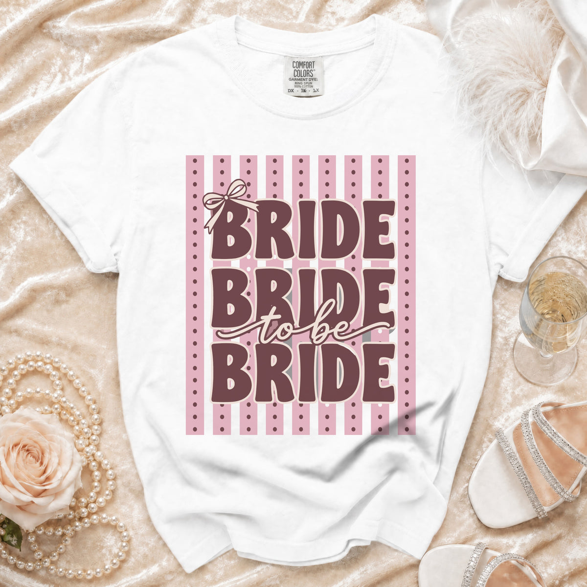 White t-shirt with "Bride to be Bride" text on a pink stripe background.