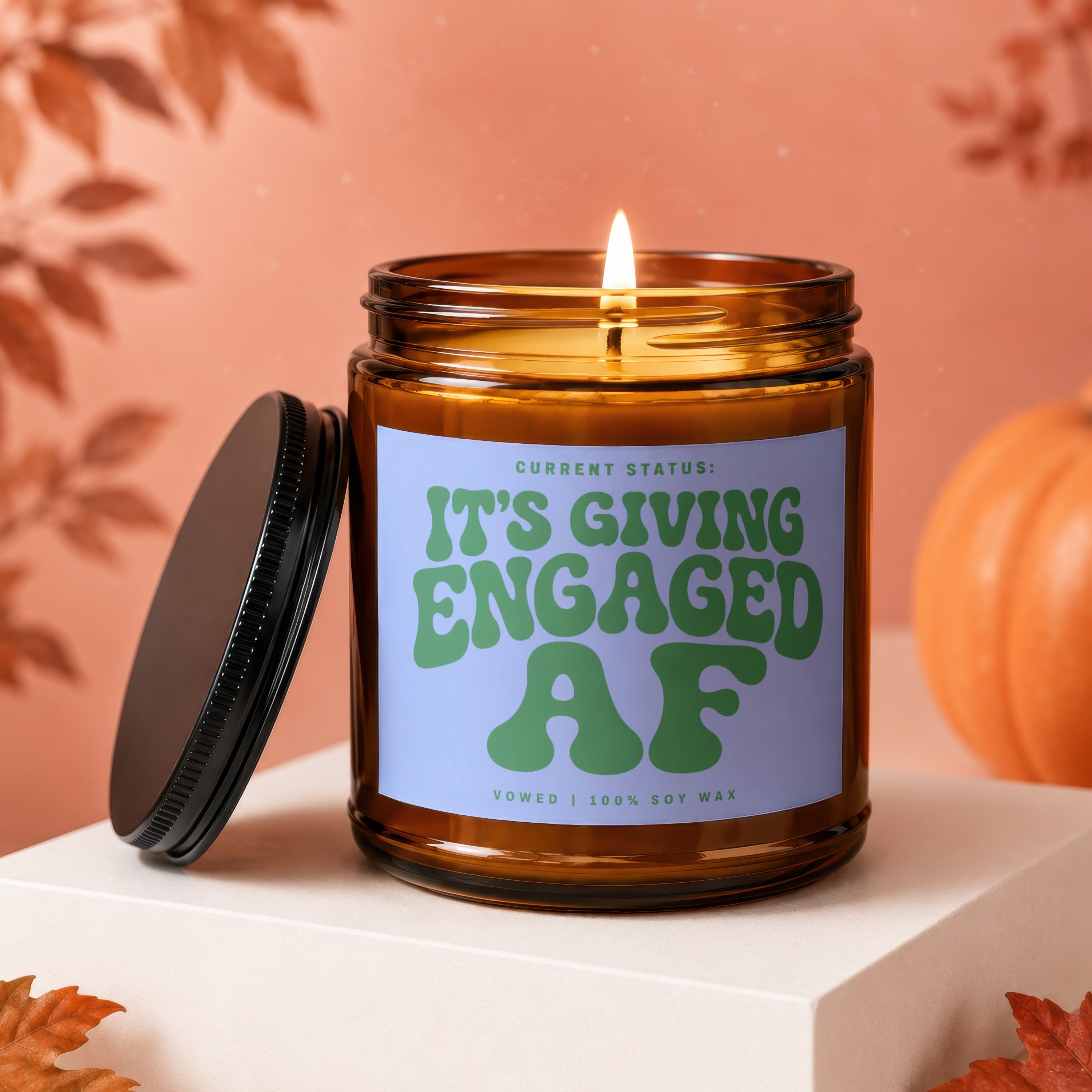 Amber jar candle with "It's Giving Engaged AF" text, lit flame, lid off.