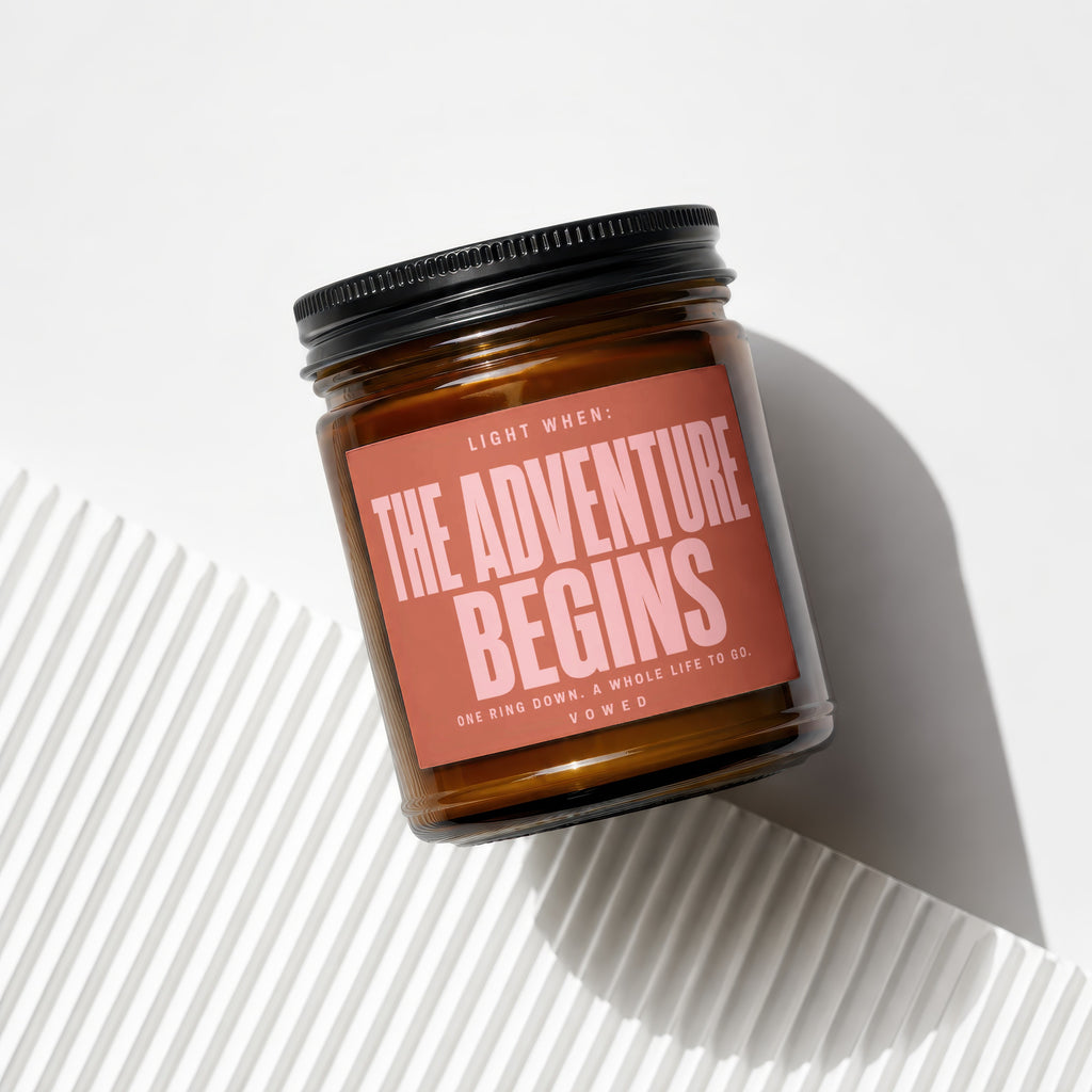 Amber candle with black lid, reads "Light When: The Adventure Begins"