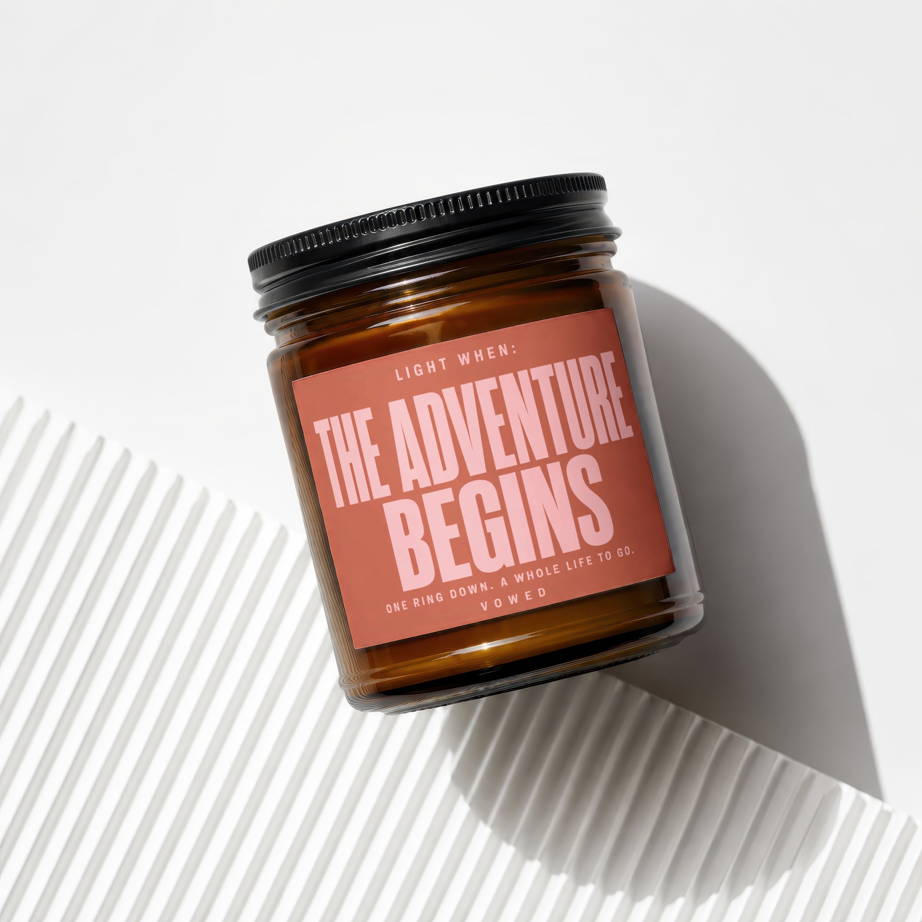 Amber candle with black lid, reads "Light When: The Adventure Begins"