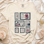 Cream t-shirt with postage stamp graphics: "Spookily Single," "Ghouls Just Wanna Have Fun," "Haunted Honeymoon," "Til Death Do Us Party," "Boo-tiful Bride," "Drink Up Witches," and "Pumpkin the Vows."