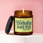 Amber glass candle with lit wick and cap removed, label reads "Both of us said yes".