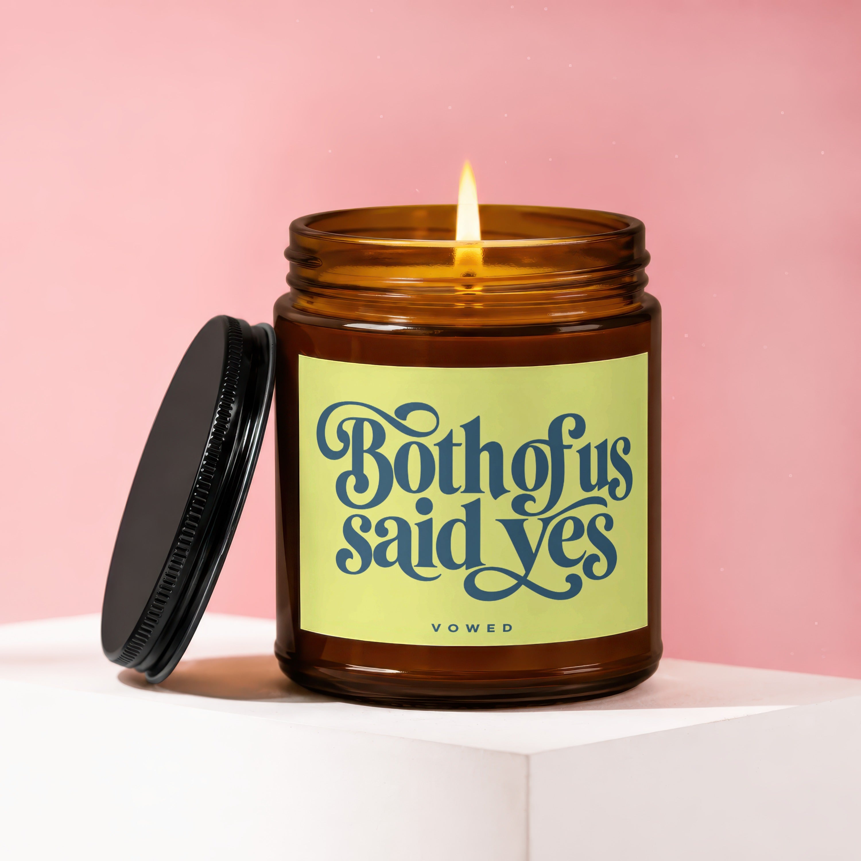Amber glass candle with lit wick and cap removed, label reads "Both of us said yes".