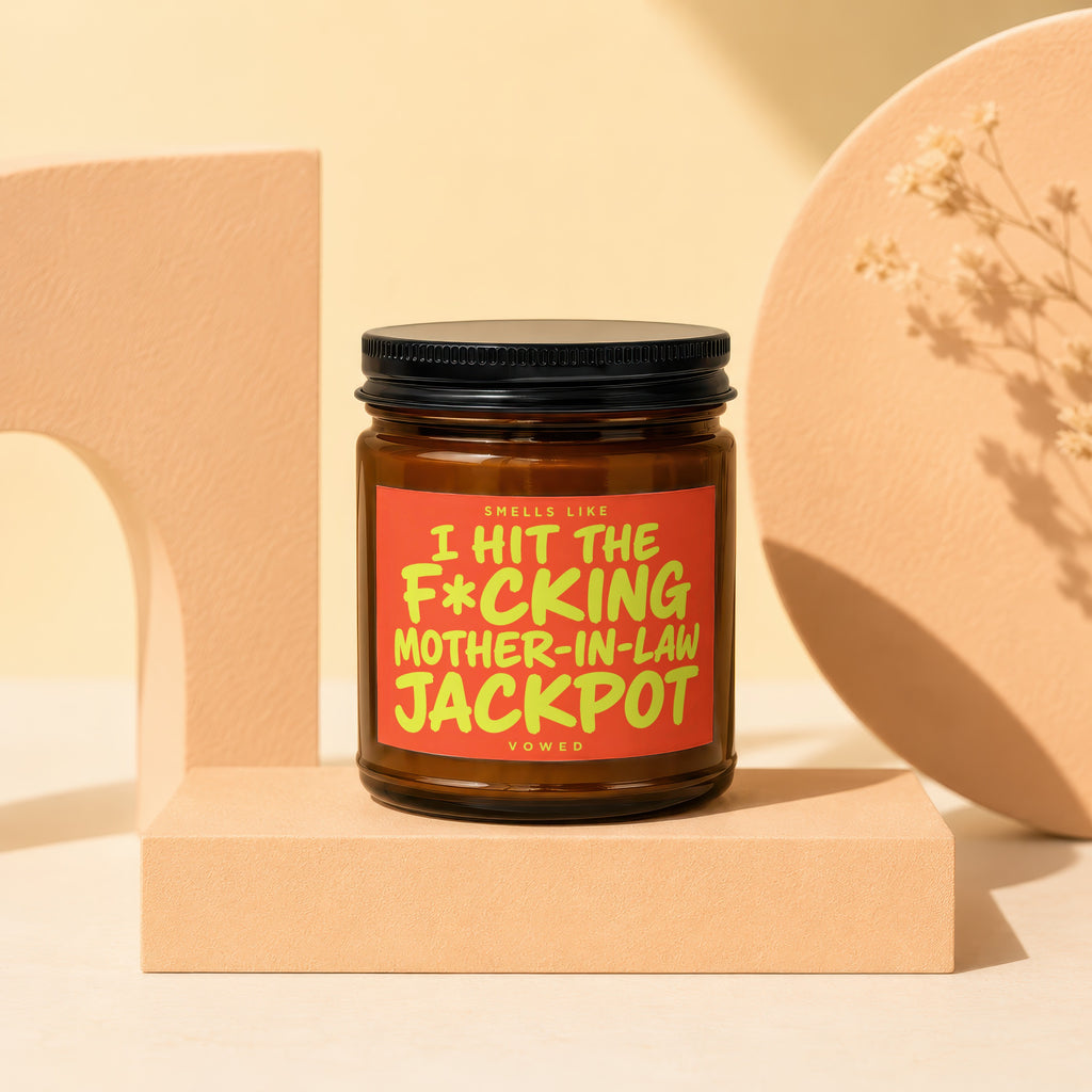 Brown candle with a black lid, featuring a label that says "Smells Like I Hit The F*cking Mother-In-Law Jackpot".