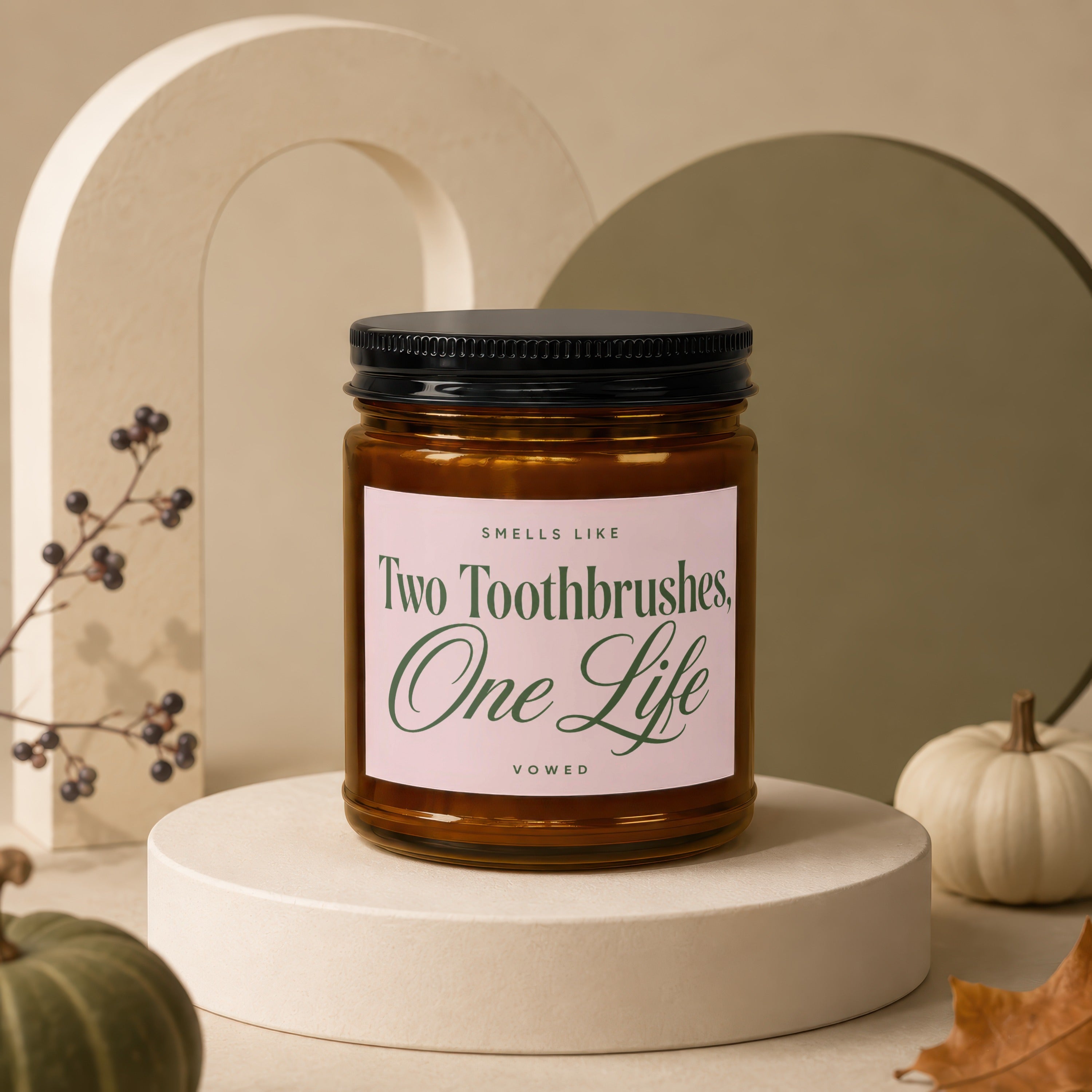 Amber jar candle with pink label reading "Smells Like Two Toothbrushes, One Life, Vowed."