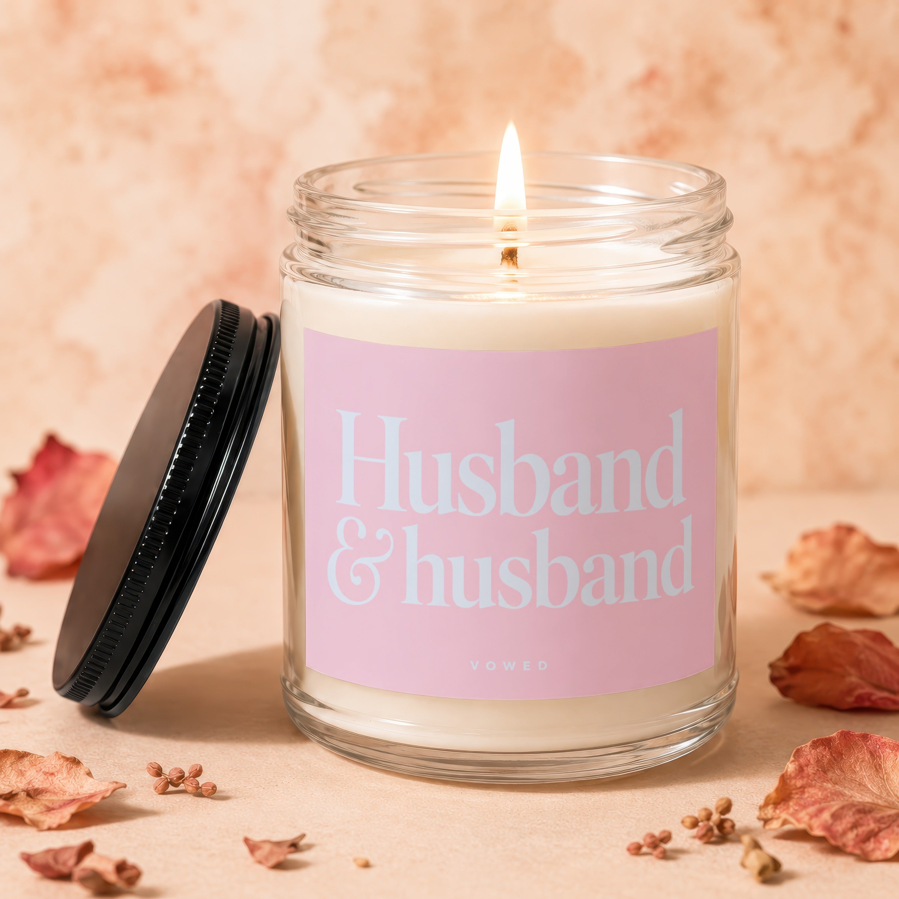 Lit glass candle with pink label reading "Husband & husband, vowed".
