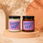 Two candles with "Wifed Up" text on pink labels, displayed on a beige platform.