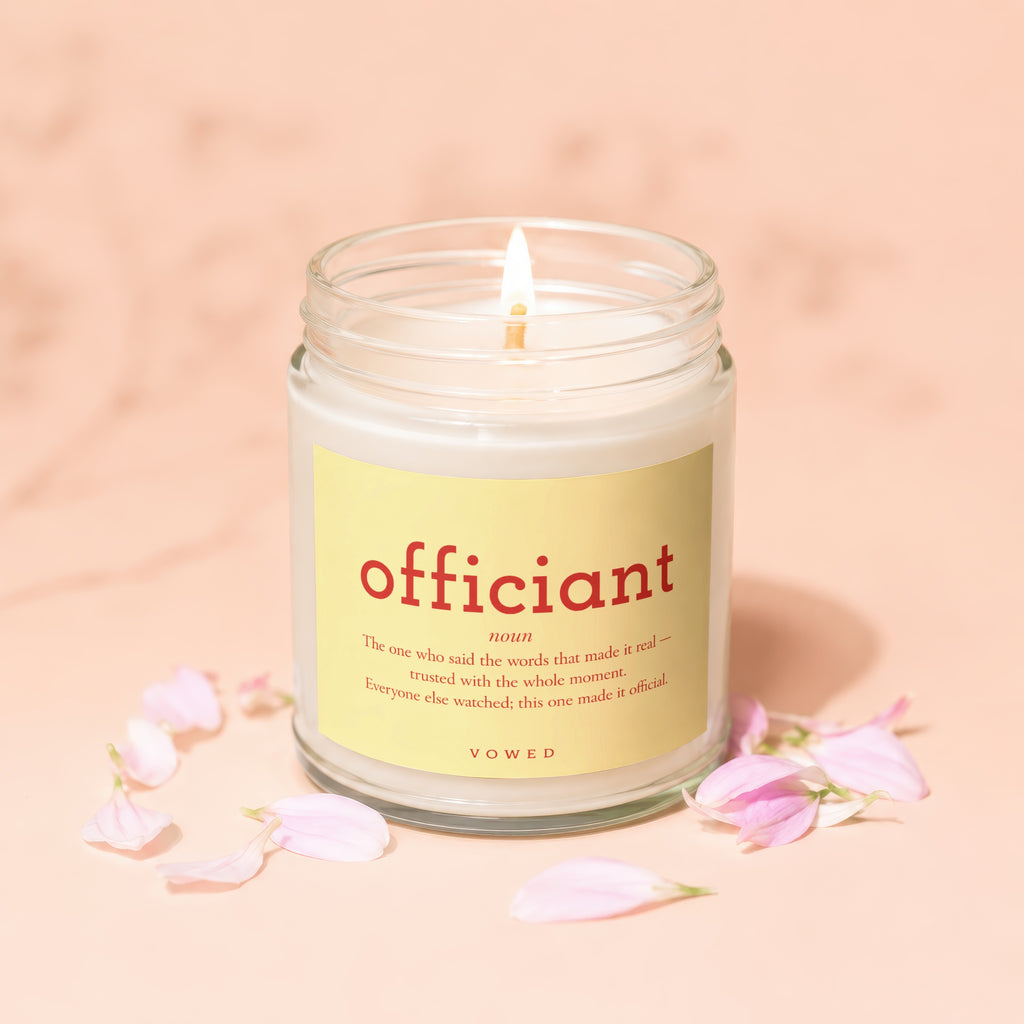Candle with "officiant" definition and "VOWED" on label, surrounded by petals.