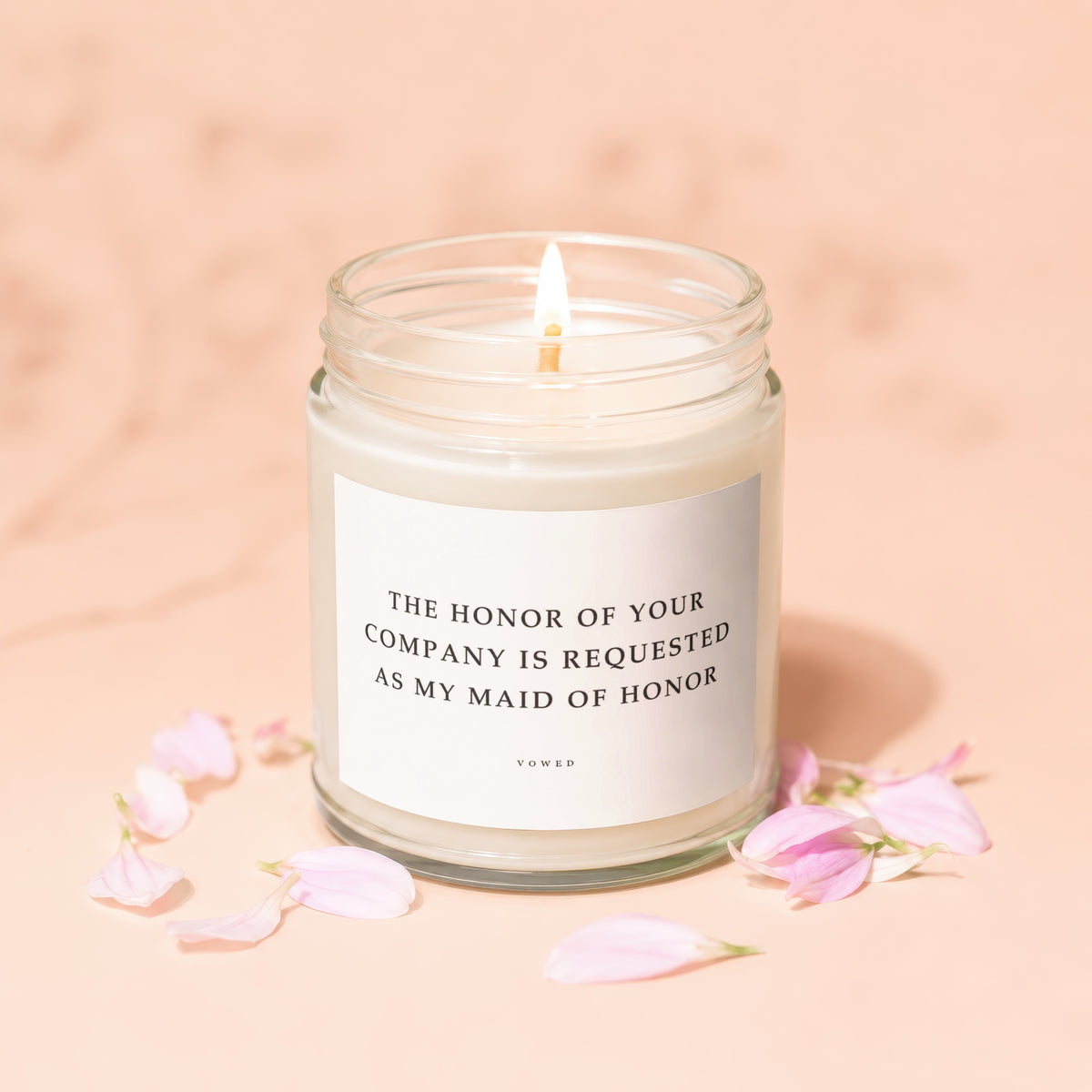Jar candle with lit wick and pink petals, reading "The honor of your company is requested as my maid of honor."