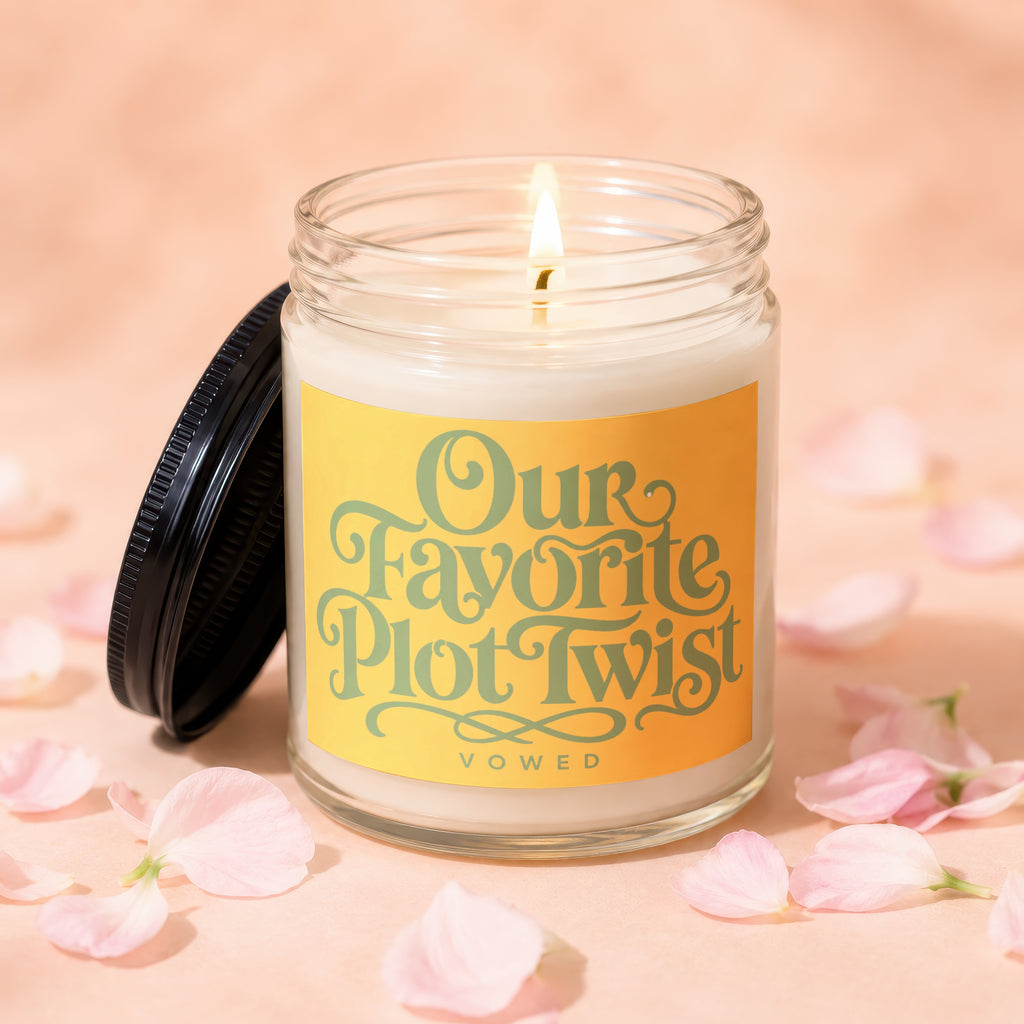 Glass jar candle with lit wick and yellow label inscripted "Our Favorite Plot Twist VOWED".
