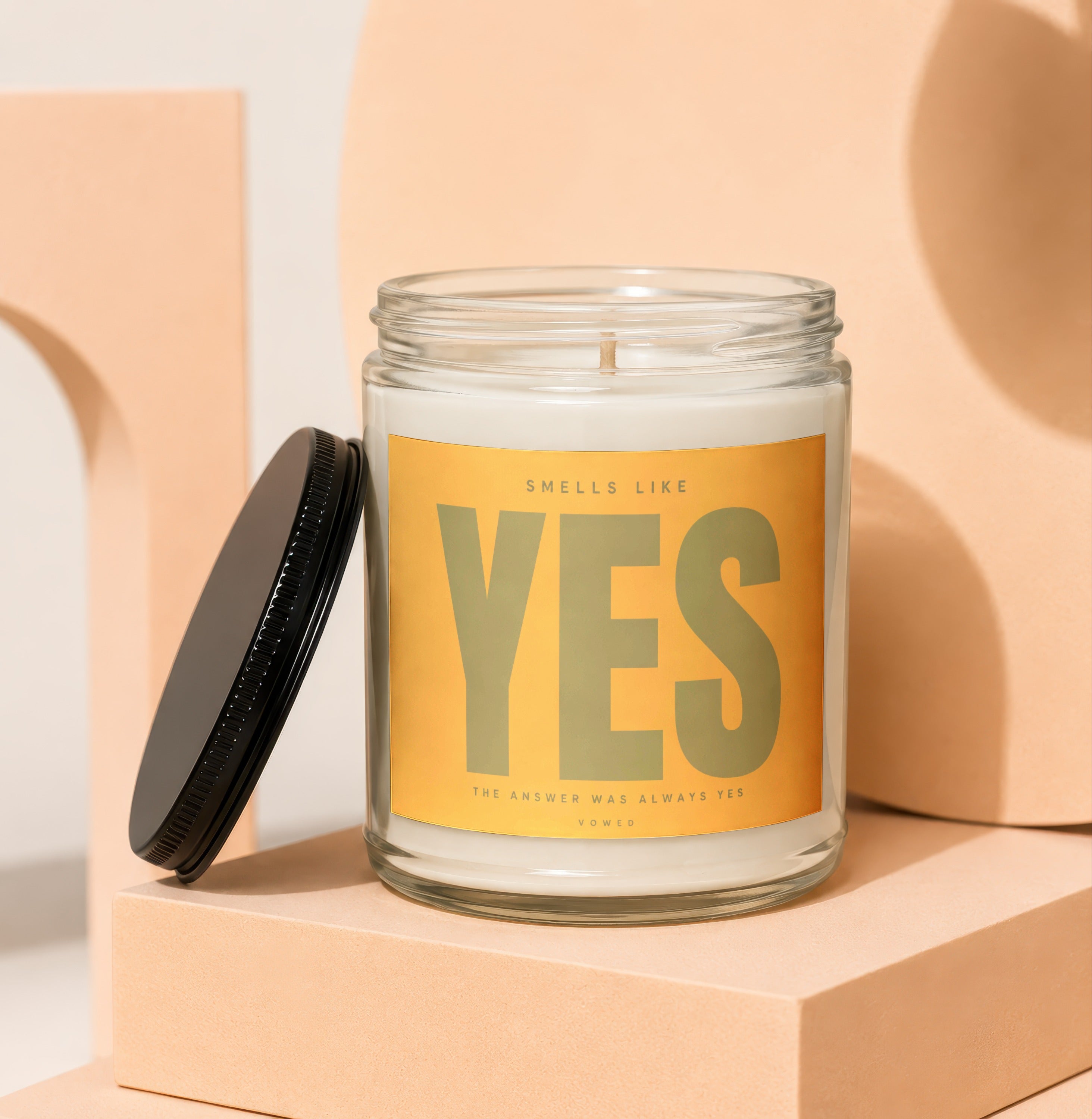 Glass candle with a yellow label reading "SMELLS LIKE YES THE ANSWER WAS ALWAYS YES VOWED".