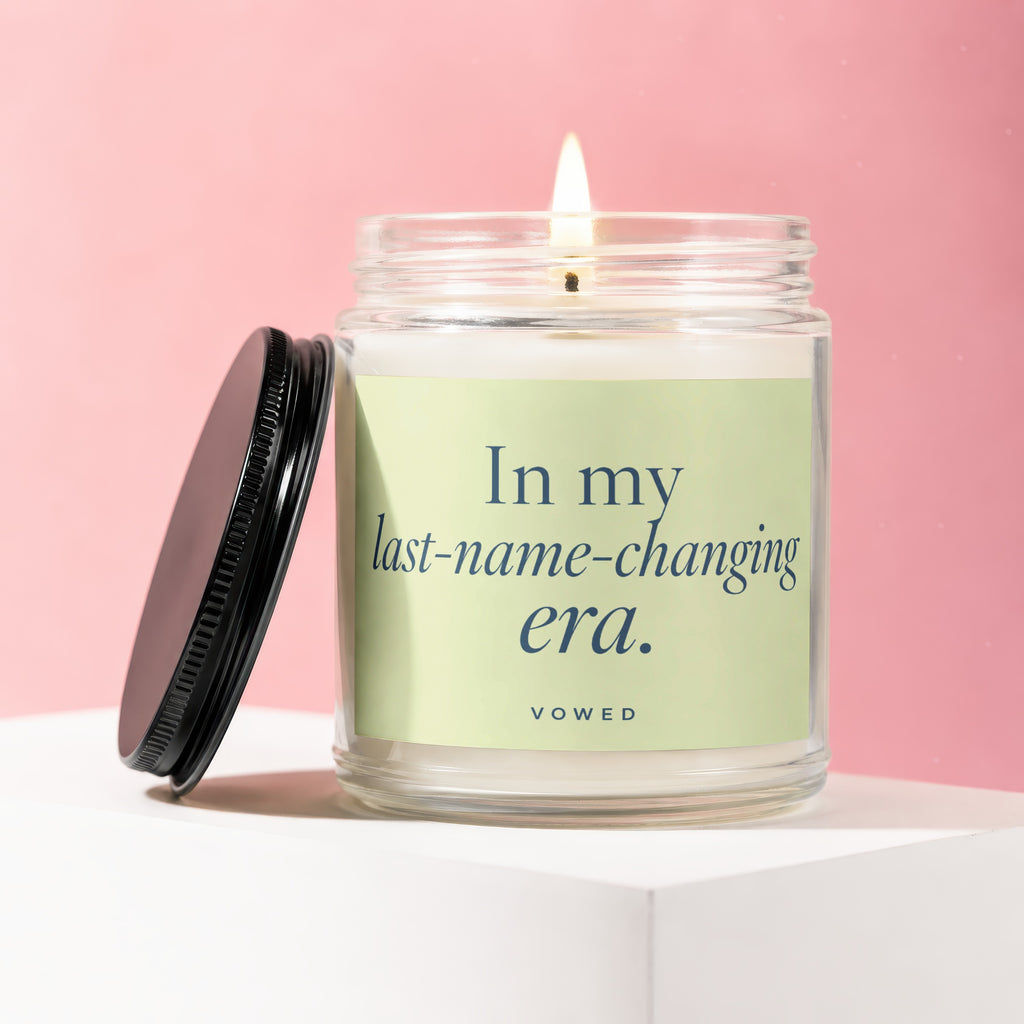 Candle in glass jar with lit wick and black lid off to the side with text "In my last-name-changing era."
