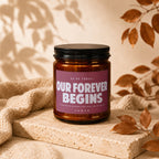Amber candle with a pink label reading "OUR FOREVER BEGINS".